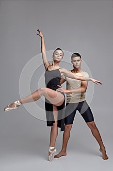 Two athletic modern ballet dancers are posing against a gray studio background.