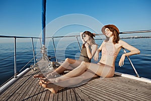 Two attractive adult woman on yacht, sailing in sea and sunbathing on bow of boat, feeling relaxed and pleased. Hot