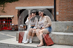 Two attractive Asian female friends are sitting on the stairs in the city with their shopping bags