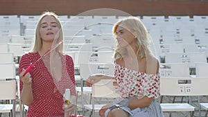 Two attractive beautiful young blond women blow bubbles in the park and are happy on sunset. Girlfriends in park. Slow motion