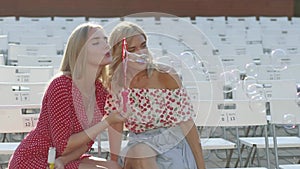 Two attractive beautiful young blond women blow bubbles in the park and are happy on sunset. Girlfriends in park. Slow motion