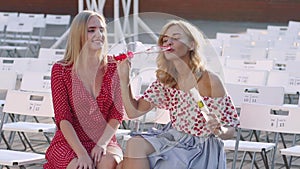 Two attractive beautiful young blond women blow bubbles in the park and are happy on sunset. Girlfriends in park. Slow motion