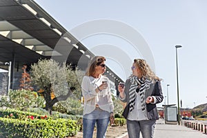 Two attractive business women are walking while having a coffee and chatting