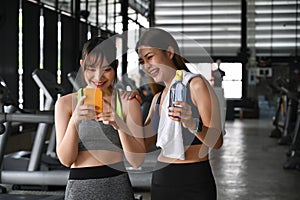 Two fitness woman taking a break after workout and using smart phone.