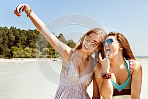 Two attractive girl standing together, posing and doing selfie beach