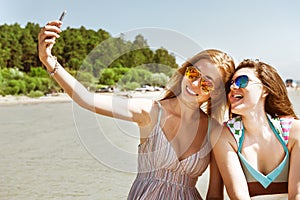 Two attractive girl standing together, posing and doing selfie beach