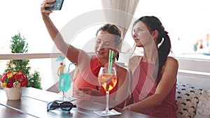 Two attractive girlfriends having fun and making selfie in restaurant on the seashore in summer weekend.