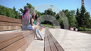 Two attractive girlfriends talking to each other having a good mood sitting on a bench in the park