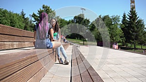 Two attractive girlfriends talking to each other having a good mood sitting on a bench in the park. 4K