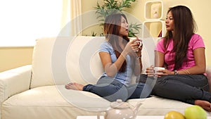 Two attractive happy sisters sitting on couch holding mugs