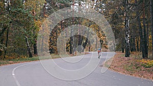 Two attractive male triathletes are training on road bike in autumn park. Young cyclists in sportswear and helmets riding on bicyc