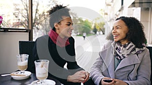 Two attractive mixed race women talking and drinking coffee in street cafe. Friends have fun after visiting mall sale