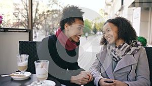 Two attractive mixed race women talking and drinking coffee in street cafe. Friends have fun after visiting mall sale