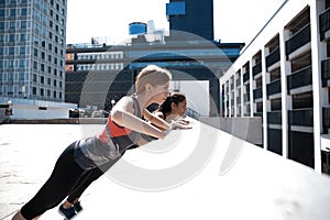 Two attractive sport girls smiling while working out and doing push-ups in street city