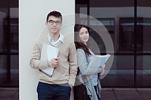 Two attractive students talking and looking in folder Outside Building at campus