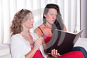 Two attractive woman siiting on couch discussing and taking note