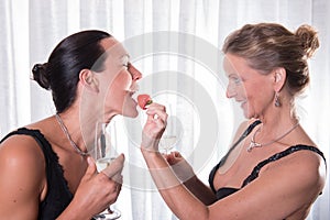 Two attractive women - one is feeding the other with strawberry