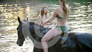 Two attractive women ride on the horses in the river at sunset