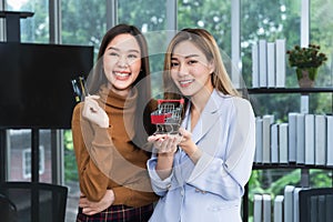 Two attractive and young Asian women hold simulated credit cards and shopping carts with smiles.