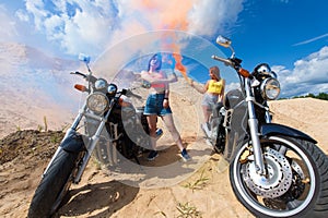 Two attractive young girls on motorbikes with smoke bombs