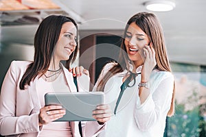 Two attractive young women looking at the tablet screen together and talking on mobile phone
