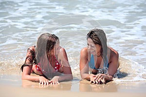 Two attractive young women lying on a sunny beach near the water