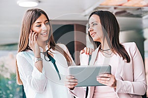 Two attractive young women sharing ideas on a digital tablet and talking on mobile phone