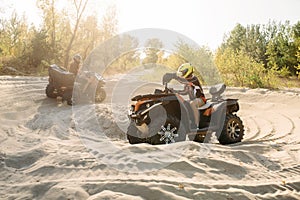 Two atv riders in helmets ride in a circle on sand