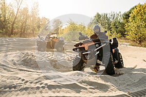 Two atv riders in helmets ride in a circle on sand