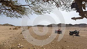 Two ATVs in the desert on a background of hills and mountains on a sunny hot day