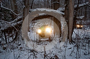 Two ATVs on wheels with headlights on ride through a snowy forest.