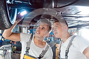 Two auto mechanics analyzing the rims of a lifted car