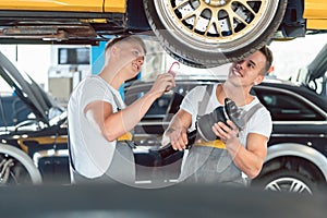 Two auto mechanics analyzing the rims of a lifted car