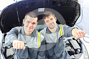 Two auto mechanics examining car with open hood