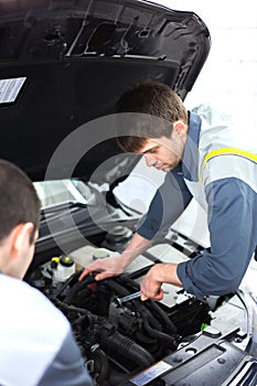 Two auto mechanics examining car with open hood