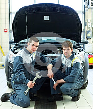 Two auto mechanics examining car with open hood