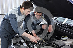 Two auto mechanics examining car with open hood