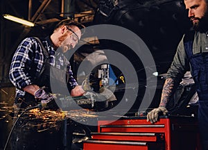 Two b mechanics working with an angle grinder in a garage.