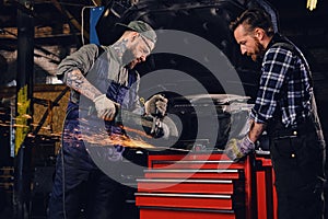 Two b mechanics working with an angle grinder in a garage.