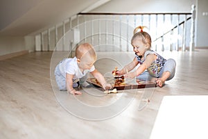 Two babies boy and girl playing chess on the white wooden floor at home