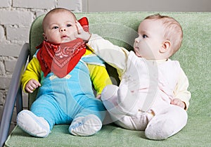 Two babies sitting on a sofa together