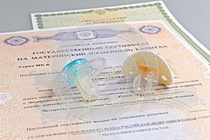 Two baby's dummies with maternal and birth certificates on gray