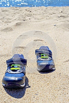 Two baby shoes on the beach and footprints in the sand