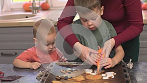 two baby sibling brothers learning to decorate halloween cookies with mother