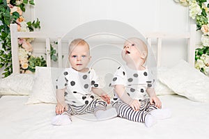 Two baby twins 8 months old sitting on the bed in the same clothes, brother-sister relationship, fashionable clothes for children