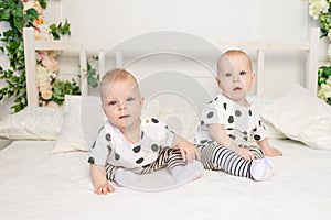 Two baby twins 8 months old sitting on the bed in the same clothes, brother-sister relationship, fashionable clothes for children