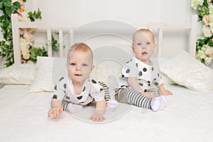 Two baby twins 8 months old sitting on the bed in the same clothes, brother-sister relationship, fashionable clothes for children