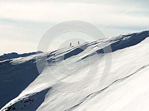 Two backcountry skiers hiking up on a long mountain ridge towards the summit near Klosters in the Swiss Alps in deep winter