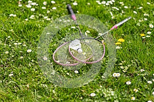 Two badminton rackets and a shuttlecock lie on the green grass.