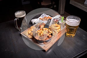 Two bakals of beer, dark and light, snacks for beer. Fried chicken legs, onion rings, cheese balls, fried vareniki and